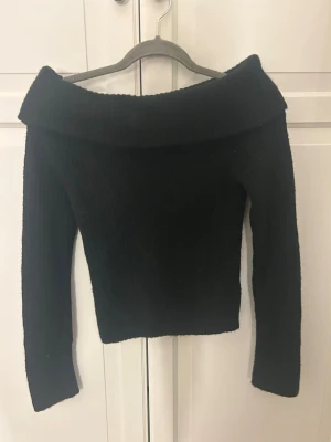 Svart offshoulder topp från H&M - Säljer en svart offshoulder topp från H&M i storlek XS. Toppen har lång ärm och en bred, nedvikt krage som ger en snygg och trendig look. Perfekt att styla med höga jeans eller kjol för en cool outfit.