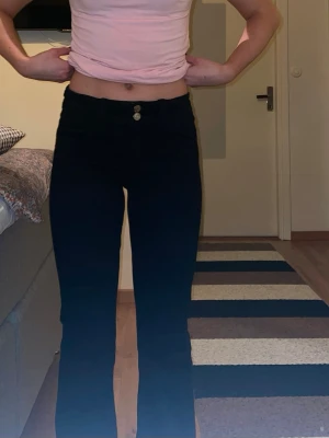 Svarta bootcut jeans med medel midja - Säljer ett par svarta bootcut jeans med mellan midja och dubbla knappar framtill. Jeansen har en smickrande passform och lätt utsvängda ben. 
