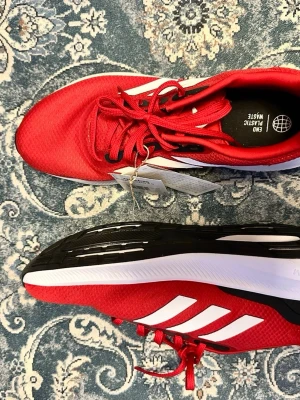 Adidas Runfalcon 3.0 röda sneakers - Snygga röda Adidas Runfalcon 3.0 sneakers med vita och svarta detaljer. Ovandelen är i mesh för bra andningsförmåga och sulan har Cloudfoam-dämpning för extra komfort. Klassiska tre vita ränder på sidan och röda skosnören. Perfekta för en sportig look.