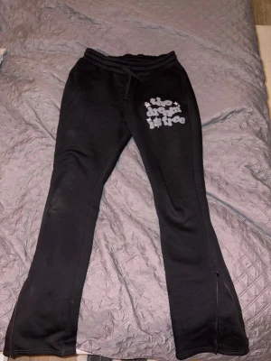 Svarta mjukisbyxor med slits Lorenzo veratti  - Svarta mjukisbyxor med tryck. Byxorna har utsvängda ben med slits nertill och resår i midjan med dragsko. Mjukt material som är perfekt för en avslappnad stil.