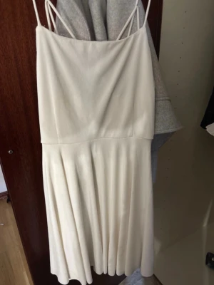 Vit kortklänning med tunna axelband - Säljer en stilren vit kortklänning med tunna axelband och vidd i kjolen. Klänningen har en enkel, elegant design med smala band som korsas i ryggen. Perfekt för sommarens alla tillfällen.