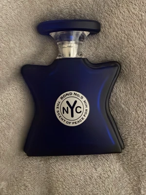 Bond No. 9 The Scent of Peace for Him - En exklusiv herrparfym från Bond No. 9 i en djupblå, stjärnformad flaska med silverdetaljer och tydlig NYC-logga på framsidan. Flaskan har en unik, modern design och är tillverkad i glas med en elegant plastkork. Låda kommer med
