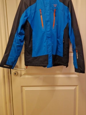 Blå och svart vindjacka Tenson - Snygg blå och svart skidjacka från Tenson.Materialet är slitstarkt och vattenavvisande, perfekt för blåsiga dagar. 