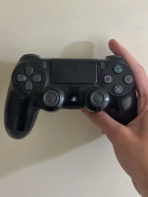 PS4 Kontroll - Säljer en svart DualShock 4 handkontroll till PlayStation 4. Den har klassisk layout med två analoga spakar, touchpad, och de ikoniska PlayStation-knapparna i färg. Tillverkad i plast med en skön form som ligger bra i handen. Perfekt för gaming och multiplayer-sessioner.