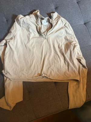 Beige långärmad tröja från ICIW - Beige långärmad tröja från CMP med halv dragkedja framtill och hög krage. Tillverkad i ett mjukt och lätt material, perfekt för lager-på-lager. Diskret logga på bröstet och enkel, avslappnad passform.