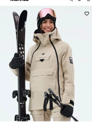 Beige regnjacka från Montec - Snygg beige vindjacka från Montec med svart dragkedjedetalj och stor ficka framtill. 