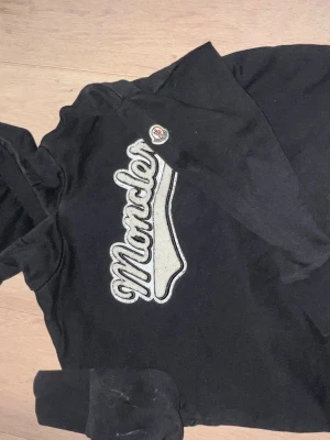 Svart Moncler hoodie med logga - Säljer en svart hoodie från Moncler med stor broderad logga i vitt och grått på bröstet samt Moncler-märke på ärmen. Hoodien har klassisk huva och ribbade muddar. Perfekt för dig som gillar streetwear och vill ha något stilrent men ändå lyxigt. Denna hoodie är lite konstig i sizen så fråga hjärna inan ni köper !👌🏽
