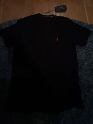 Svart t-shirt från Polo Ralph Lauren - Klassisk svart t-shirt från Polo Ralph Lauren med liten röd logga broderad på bröstet. T-shirten har rund hals och korta ärmar, perfekt för en clean och stilren look. Tillverkad i mjuk bomull för skön känsla hela dagen.