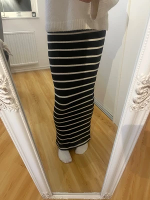 Svartvit randig långkjol - Snygg långkjol med svarta och vita horisontella ränder. Kjolen har en rak passform och är tillverkad i ett stretchigt, ribbat material som sitter skönt mot kroppen. Perfekt för dig som gillar en stilren och trendig look.