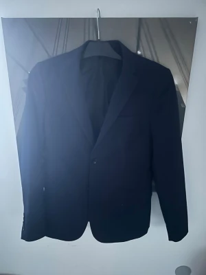 Klassisk mörkblå kavaj - Snygg mörkblå kavaj med dubbelknäppning och smal passform. Kavajen har två framfickor, bröstficka och knappar vid ärmsluten. Perfekt för en stilren och modern look.