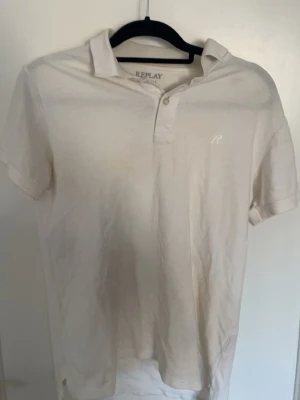 Vit piké från Replay med krage - Klassisk vit pikétröja från Replay med korta ärmar, krage och knappar framtill. Tröjan har en diskret broderad logga på bröstet och är tillverkad i mjuk bomull. Perfekt till en avslappnad och stilren look.