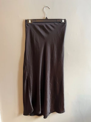 Svart satinkjol i lång modell - Säljer en stilren svart långkjol i satin med lätt glansig finish. Kjolen har en rak passform och faller snyggt längs benen. Perfekt att matcha med en enkel topp eller stickad tröja. Pris förslag tas gärna emot