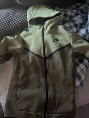 Olivgrön Nike hoodie med dragkedja - Snygg olivgrön hoodie från Nike med svart dragkedja och svarta detaljer. Hoodien har en klassisk huva och Nike-logga på bröstet. Tillverkad i mjukt och bekvämt material, perfekt för chill eller streetwear. Fickor på sidorna för extra funktion.