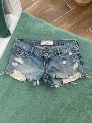 Hollister lågmidjade jeansshorts  - Ett par jeansshorts från Hollister i storlek W27, vilket motsvarar en vanlig S. Rakt över midjemått: ca 38cm.   Jag fraktar inom 24h, frakt med PostNord prioriteras. Se liknande plagg i min profil!