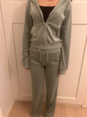 Ljusgrön Juciy couture  - Mjuk och skön hoodie i ljusgrön  velour med dragkedja framtill och huva. Tröjan har breda muddar vid ärmslut och midja samt fickor framtill. Perfekt för en avslappnad och trendig look. och ett par ljusgröna velour byxor. Är ungefär 160cm och längden är perfekt 
