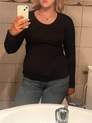 Svart långärmad topp i bomull - En enkel och stilren svart långärmad topp med rund halsringning. Toppen är figurnära och passar perfekt till jeans eller kjol. Tillverkad i mjuk bomull som känns skön mot huden. Perfekt basplagg för alla tillfällen.