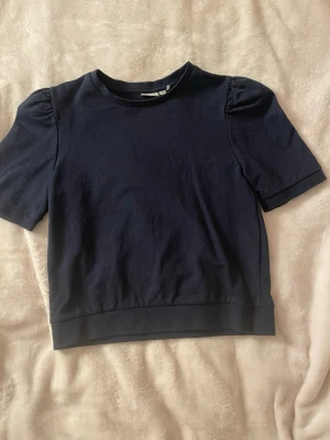 Mörkblå kortärmad topp med puffärm - En mörkblå topp med korta puffärmar och rund halsringning. Toppen är i mycket bra skick då jag inte använt den så mycket.