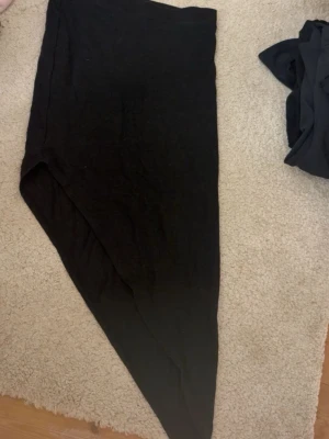 Svart asymmetrisk kjol från H&M Divided - Svart kjol från H&M Divided med cool asymmetrisk skärning. Kjolen är enkel och stilren, perfekt att matcha med olika toppar. Tillverkad i mjukt material som känns skönt mot huden.