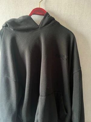 Svart Essentials hoodie - Snygg svart hoodie från Essentials Fear of God med diskret logga på bröstet och stor text på ryggen. Hoodien har en rymlig huva och känguruficka framtill. Tillverkad i mjukt bomullsmaterial som känns riktigt skönt mot huden. Perfekt för en avslappnad streetwear-look.