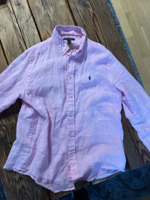 Rosa linneskjorta från Polo Ralph Lauren - Säljer en ljusrosa skjorta från Polo Ralph Lauren i linne. Skjortan har klassisk krage, knappar framtill och den ikoniska broderade loggan på bröstet. Perfekt för dig som gillar en avslappnad men ändå stilren look. Pris kan diskuteras. Storlek L i barn storlek. Passar folk som är 168-178