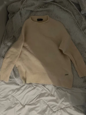 Beige stickad tröja Polo Ralph Lauren - Säljer en stilren beige stickad tröja från Polo Ralph Lauren. Tröjan har rund halsringning, breda ribbstickade muddar vid ärmslut och nederkant samt en liten metallbricka vid fållen. Perfekt för lager på lager och enkel att matcha.