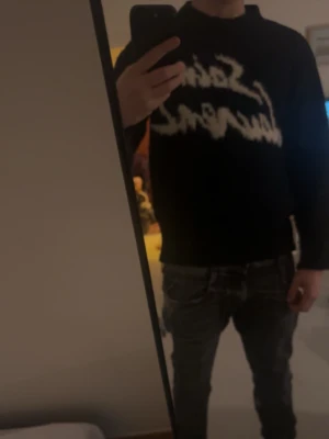YSL tröja - Säljer en svart tröja med vit, stor text på bröstet i en cool, handskriven stil. Tröjan har rund hals och långa ärmar. Perfekt för dig som gillar streetwear och vill sticka ut lite extra.