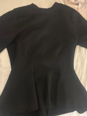 Svart figursydd tröja  - Snygg svart tröja med figursydd passform och lätt utsvängd nederdel. Klassisk modell som ger en stilren siluett. Perfekt att matcha med både jeans och kostymbyxor för en trendig look.