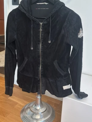 Odd molly - Säljer en svart hoodie från odd Molly i mjuk velour med dragkedja framtill och fickor. Huvan har dragsko och på ena ärmen finns en vit broderad detalj med text och bladmotiv. Perfekt för en chill och avslappnad stil.