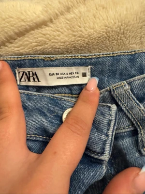 Blå bootcut jeans från Zara - Säljer ett par ljusblå bootcut jeans från Zara med klassisk femficksdesign och hög midja. Jeansen har en snygg tvätt och är tillverkade i ett mjukt denimtyg som sitter skönt. Perfekta för dig som gillar en retroinspirerad look.