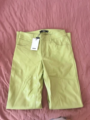 Limegröna skinbyxor från Bik Bok - Säljer ett par trendiga limegröna skinbyxor från Bik Bok. Modellen har raka ben, klassisk femficksdesign och knappgylf. Materialet är mjukt och har en lätt glansig finish som sticker ut. Perfekta för dig som vill ha en färgklick i garderoben!