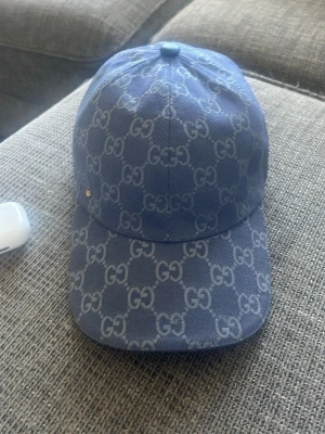 Blå GG-mönstrad keps  - Snygg blå keps från  med det klassiska GG-monogrammet över hela kepsen. Justerbar rem bak och böjd skärm. Tillverkad i ett slitstarkt tyg med vit insida och märkestag på insidan. Perfekt för dig som vill ha en exklusiv och trendig accessoar kan gå ner i pris vid snabbt köp😁