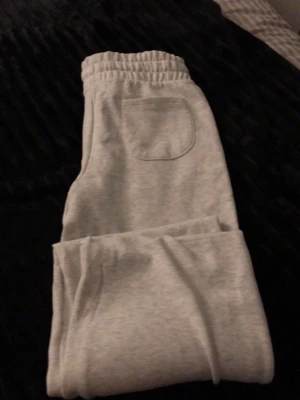 Grå mjukisbyxor med fickor - Säljer ett par ljusgrå mjukisbyxor med resår i midjan och praktiska fickor både fram och bak. Byxorna har en avslappnad passform och är tillverkade i mjukt sweatshirtmaterial, perfekta för chill dagar hemma eller när du vill vara bekväm. Byxorna är från lager 157 och är i storlek S, dem är splitternya och inte ens använda.