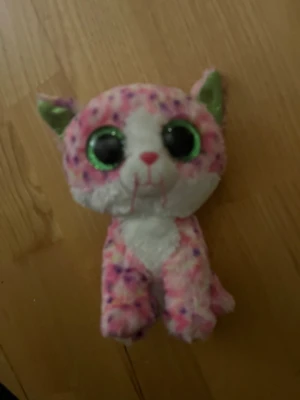 Mjukisdjur katt med stora ögon - Söt mjukiskatt i rosa, vitt och lila med stora glittriga gröna ögon och rosa nos. Katten har gröna insidor på öronen och är gjord av mjukt plyschmaterial. Perfekt som gosedjur eller dekoration i rummet.