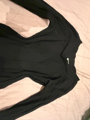 Svart ribbad långärmad tröja - Snygg svart långärmad tröja med ribbad struktur och bred krage. Tröjan har en kroppsnära passform och är perfekt för lager på lager. Passar till både jeans och kjol för en stilren look.