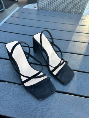 Svarta pumps med remmar från H&M - Stilrena svarta pumps från H&M med fyrkantig tå och tunna remmar över foten. Skorna har en bred klack och ovandelen är i mockaimitation. Perfekta för dig som gillar trendiga och minimalistiska skor. Använda en gång