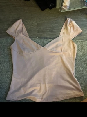 Ljusrosa v-ringad topp - Snygg ljusrosa topp med v-ringad urringning och korta ärmar. Toppen har en figurnära passform och är tillverkad i mjukt bomullsmaterial. Perfekt att styla med jeans eller kjol för en trendig look.