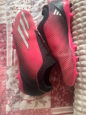 Adidas röda och svarta fotbollsskor - Säljer ett par snygga fotbollsskor från Adidas i rött och svart med vita detaljer. Skorna har en strumpliknande passform utan snörning och ovandel i mesh för bra ventilation. Perfekta för dig som vill ha stilrena och bekväma skor på planen.