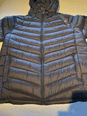 Mörkblå dunjacka från Stone Island - Snygg mörkblå dunjacka från Stone Island med huva och dragkedja framtill. Jackan har det klassiska Stone Island-märket på ärmen och horisontella sömmar som ger en cool look. Perfekt för kalla vinterdagar och riktigt skön att bära.