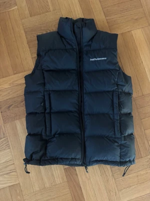 Svart dunväst från Peak Performance - Snygg svart dunväst från Peak Performance med hög krage och dragkedja framtill jätte härlig väst och har inga skador på något sätt på sig