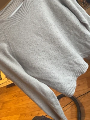 Beige stickad tröja Vero Moda - Ljusgrå stickad tröja från Vero Moda med rund halsringning och ribbade muddar vid ärmslut och nederkant. Tröjan har en enkel och klassisk design som passar till det mesta. Perfekt för lager på lager under kyliga dagar.