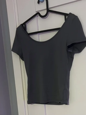 Mörkgrå croppad topp - Säljer en enkel och stilren mörkgrå croppad topp med korta ärmar och bred, djup urringning både fram och bak. Perfekt att matcha med höga jeans eller kjol för en clean look.
