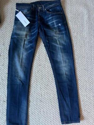 Dondup George  - Säljer ett par blå slim fit jeans från Dondup med snygga slitningar och tvättade detaljer. Jeansen har klassisk femficksmodell, normal midja och är tillverkade i denim med stretch för extra komfort. Perfekta för en trendig och avslappnad look. Storlek 32