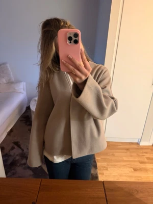 Beige vårjacka - Snygg beige jacka med minimalistisk design och rak passform. Jackan har lång ärm och dold stängning framtill, vilket ger ett stilrent intryck. Perfekt för dig som gillar enkel och clean stil.