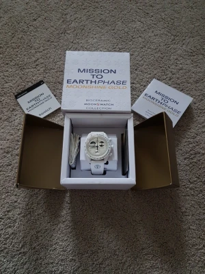 Swatch x Omega MoonSwatch Earthphase - Säljer en Swatch x Omega MoonSwatch Mission to Earthphase Moonshine Gold. Klockan är vit med blå detaljer, har biokeramisk boett och vitt armband. Urtavlan har månfasmotiv och flera subdials. Kommer med originalbox och manual.