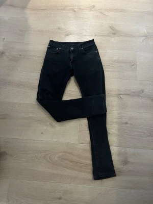 Svarta  jeans från Nudie Jeans - Snygga svarta  jeans från Nudie Jeans med klassisk femficksdesign och knappgylf. Jeansen är tillverkade i stretchigt denimtyg som sitter bekvämt. Perfekta för dig som gillar en stilren och enkel look. Pris ej hugget i en sten 