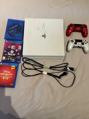 Vit PlayStation 4 Pro med kontroll - Säljer en vit PlayStation 4 Pro med två trådlösa DualShock 4-kontroller, en i röd camo och en i vitt. Medföljer HDMI- och strömkabel samt tre PS4-spel: NHL 20, Disney Infinity 3.0 och LEGO Dimensions. Perfekt för gamingkvällar med vänner. Den är lite skrapad ovanför men allt funkar som det ska. Allt på bilderna ingår.