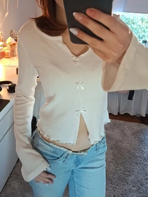 Vit ribbad topp med rosetter - Söt vit ribbad topp med lång ärm och små rosetter framtill. 