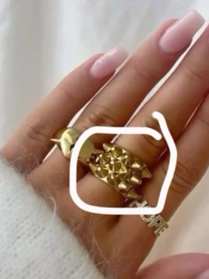 Guldig Edblad ring med nitar  - Cool ring i guldtonat metall ifrån Edblad med tre rader av konformade nitar som ger en edgy och trendig look. Ringen är bred och har en blank finish som verkligen sticker ut på fingret. Perfekt för dig som vill ha ett statement-smycke.