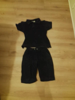 Svart set från Berns Edition - Snyggt svart set från Berns Edition med kortärmad topp och matchande shorts. Setet har en enkel och stilren design, perfekt för dig som gillar en clean look. Materialet ser ut att vara mjukt och bekvämt, och toppen har krage för extra stilpoäng.