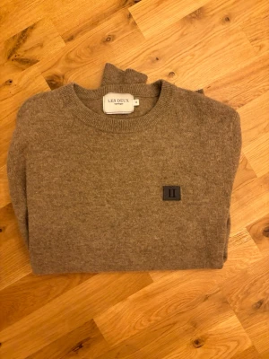 Beige stickad tröja från les deux - Stickad tröja i beige från lex deux med rund halsringning och ribbade muddar vid ärmslut och nederkant. Tröjan har en diskret logotyp-patch på bröstet och är tillverkad i mjukt material som ger en clean och stilren look.